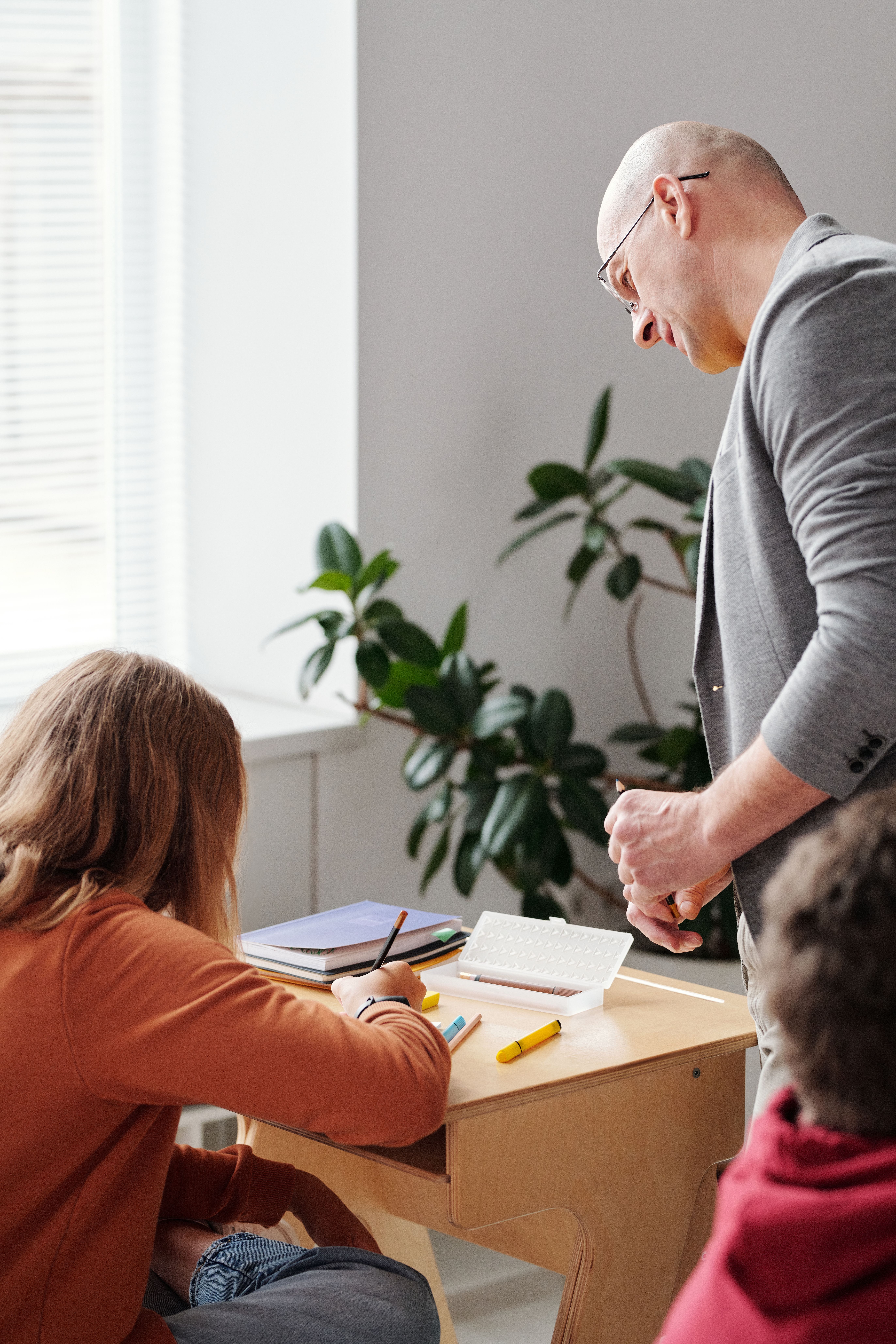 Male teacher supporting a female student with written work at a classroom desk